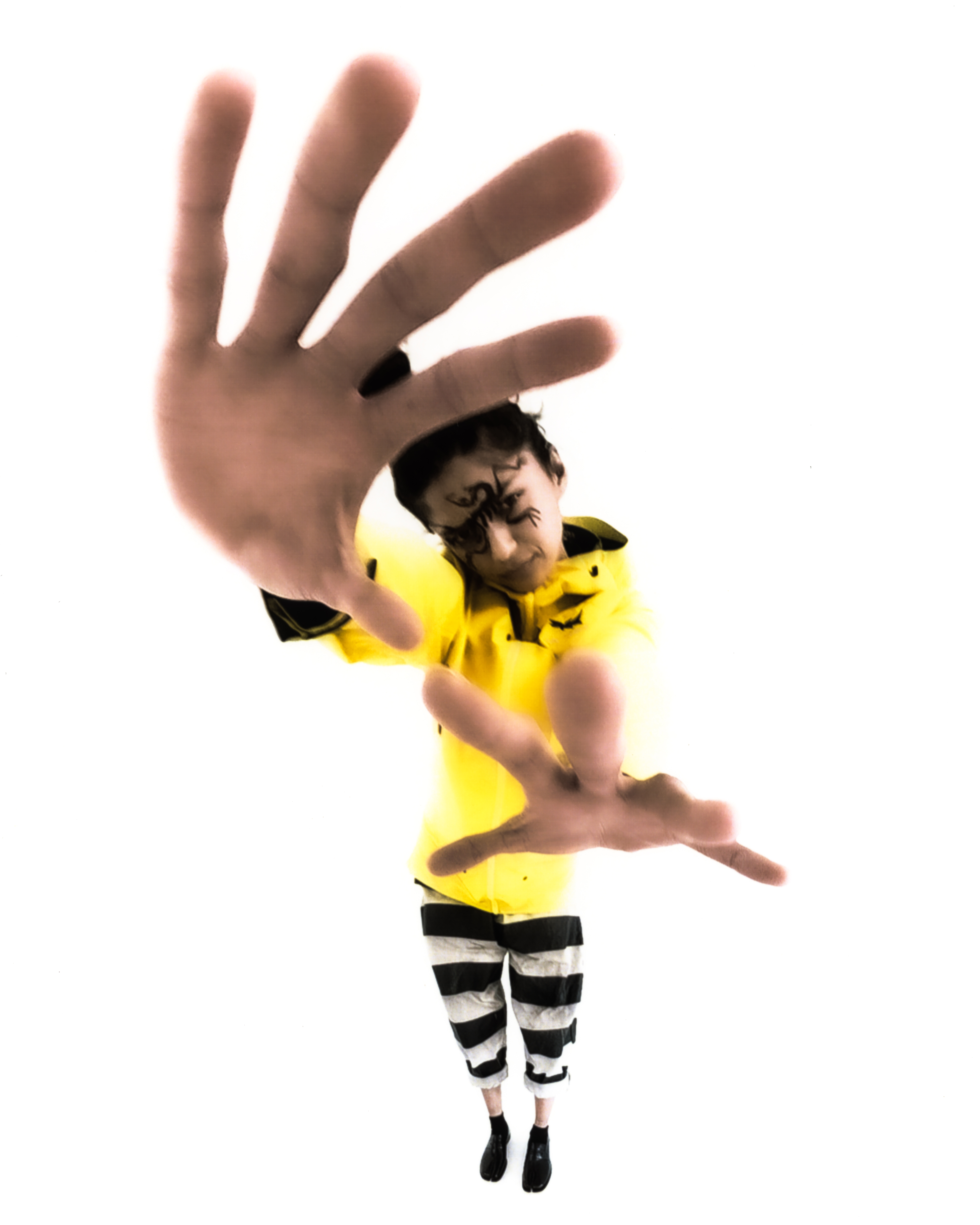 Warped image of a model with her hands facing the camera in a yellow raincoat